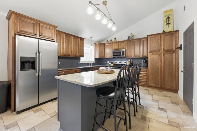 4793 Coronado Cir, Crestview, FL 32539 - kitchen with stainless steel appliances, vaulted ceiling, brown cabinetry, pendant lighting, and light stone countertops
