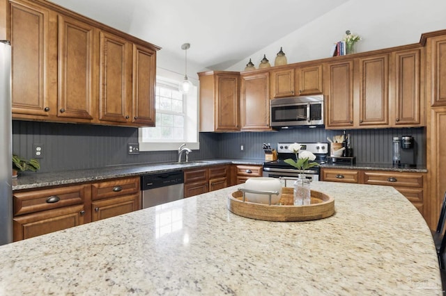 4793 Coronado Cir, Crestview, FL 32539 - kitchen featuring appliances with stainless steel finishes, brown cabinets, pendant lighting, lofted ceiling, and backsplash