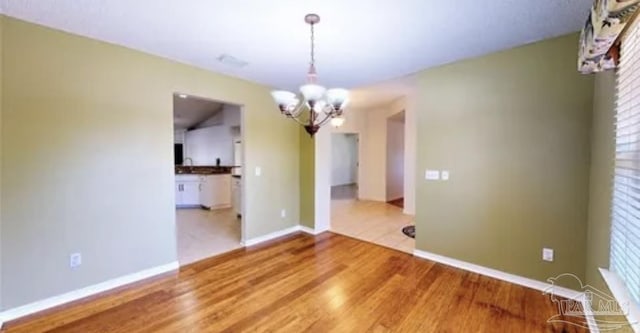 unfurnished dining area featuring an inviting chandelier, baseboards, and wood finished floors