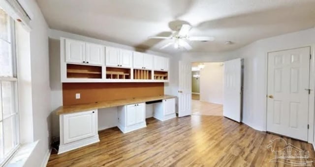 unfurnished office with a ceiling fan, built in desk, and light wood-type flooring