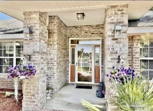 doorway to property with brick siding and roof with shingles