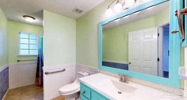 full bath featuring a wainscoted wall, toilet, vanity, tile patterned flooring, and visible vents