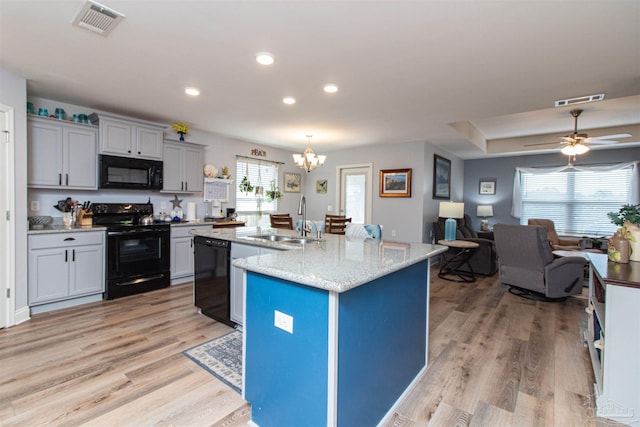 kitchen with ceiling fan with notable chandelier, light wood-type flooring, black appliances, a center island with sink, and sink