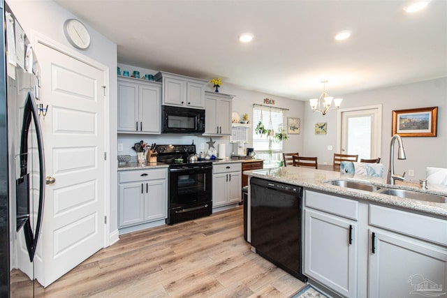 kitchen featuring light hardwood / wood-style floors, gray cabinets, black appliances, an inviting chandelier, and sink