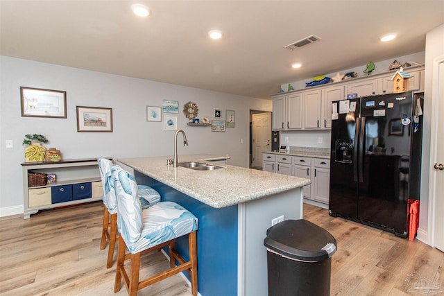 kitchen featuring a center island with sink, black fridge with ice dispenser, sink, and light hardwood / wood-style flooring