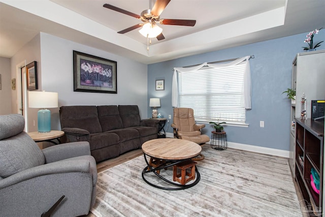 living room featuring wood-type flooring, ceiling fan, and a raised ceiling