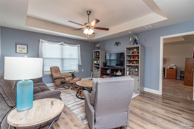 living room featuring light hardwood / wood-style floors, ceiling fan, and a raised ceiling