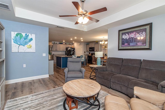 living room featuring ceiling fan with notable chandelier, light wood-type flooring, and a tray ceiling