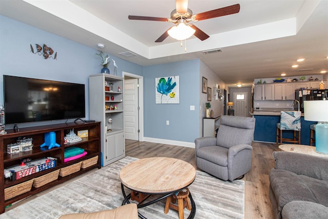 living room featuring a tray ceiling, ceiling fan, and hardwood / wood-style floors