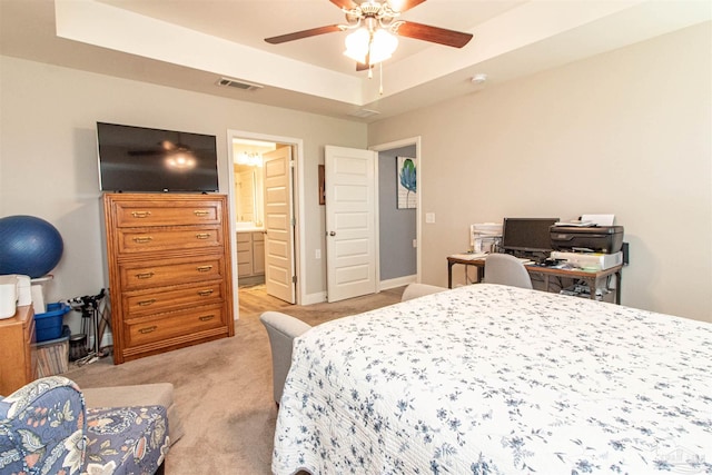 carpeted bedroom featuring a tray ceiling, ceiling fan, and ensuite bathroom