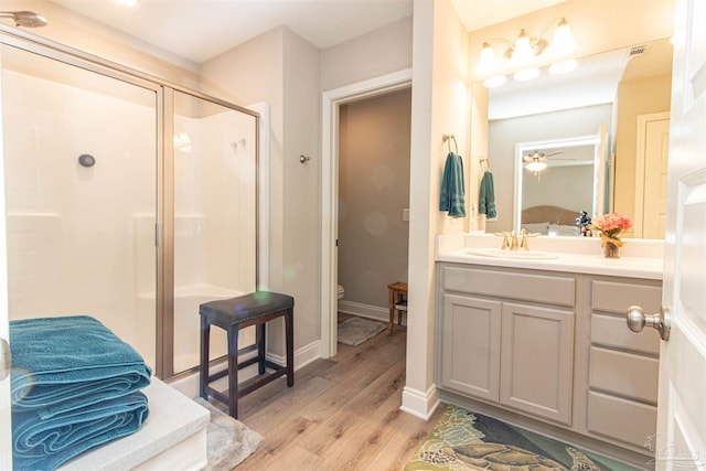 bathroom with ceiling fan, vanity, wood-type flooring, a shower with shower door, and toilet