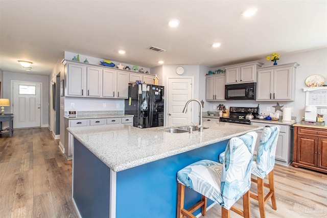 kitchen featuring light wood-type flooring, black appliances, a kitchen island with sink, and sink