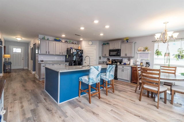 kitchen featuring a notable chandelier, light wood-type flooring, black appliances, and a center island with sink