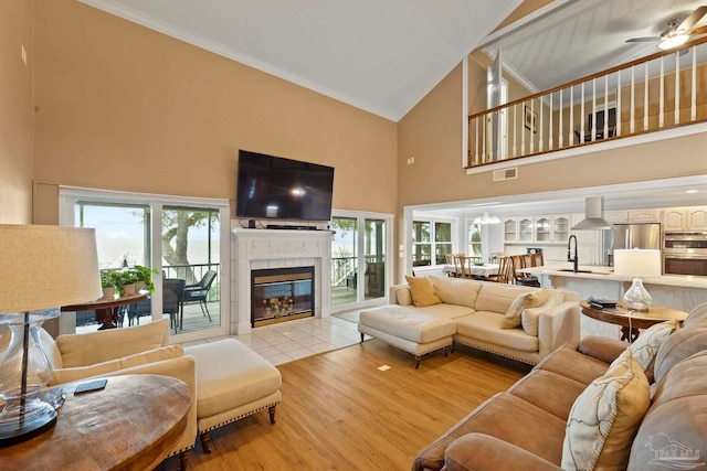 living room with ceiling fan, high vaulted ceiling, light hardwood / wood-style floors, a tile fireplace, and sink