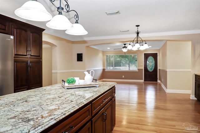 kitchen featuring hanging light fixtures, ornamental molding, stainless steel fridge, light stone countertops, and light hardwood / wood-style floors