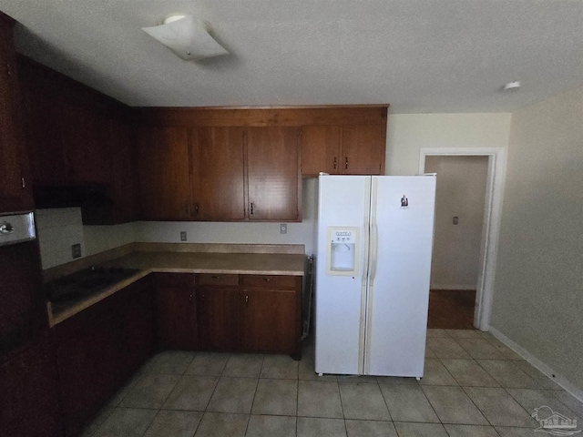 kitchen with light tile patterned flooring, white fridge with ice dispenser, and a textured ceiling