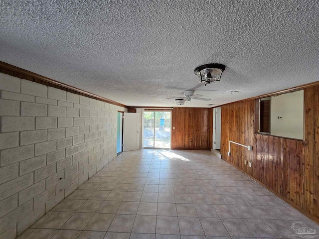 tiled empty room with wooden walls, crown molding, ceiling fan, and a textured ceiling