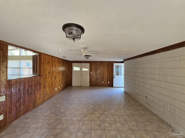 spare room with a textured ceiling, ceiling fan, wood walls, and brick wall