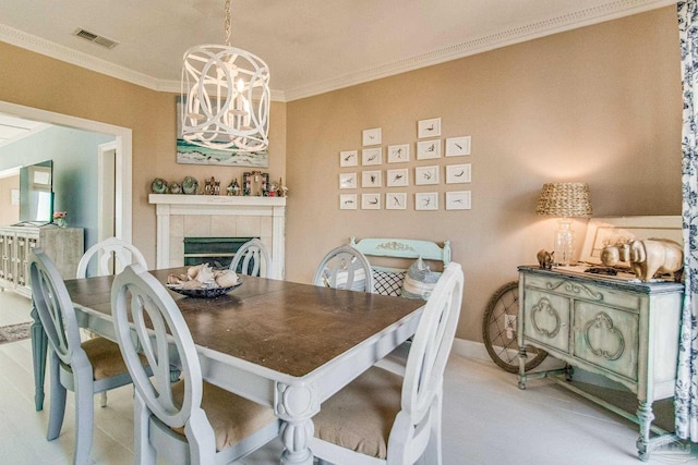 dining room with a chandelier, light tile patterned floors, crown molding, and a tiled fireplace