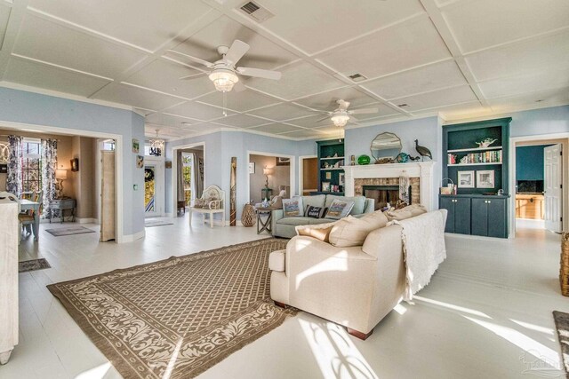 living room with built in shelves, ceiling fan, coffered ceiling, and a fireplace