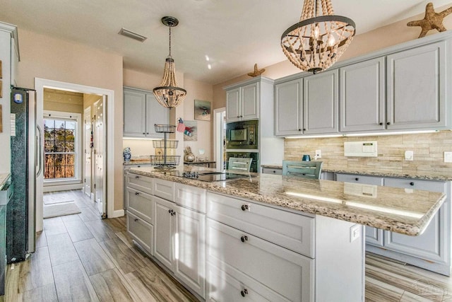 kitchen featuring black appliances, a center island, a chandelier, decorative light fixtures, and light stone counters