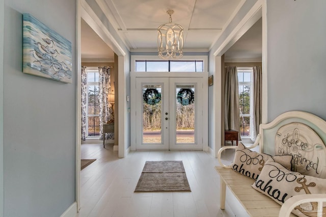 foyer with ornamental molding, a chandelier, light hardwood / wood-style flooring, and french doors