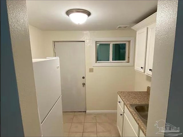 kitchen with light tile patterned flooring, light stone counters, white cabinetry, and sink