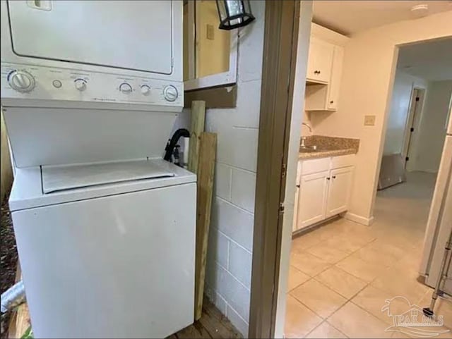 laundry room with light tile patterned flooring, sink, and stacked washer and clothes dryer