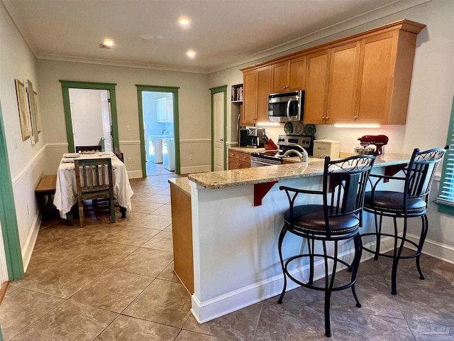 kitchen with light stone countertops, appliances with stainless steel finishes, washing machine and dryer, crown molding, and light tile patterned floors