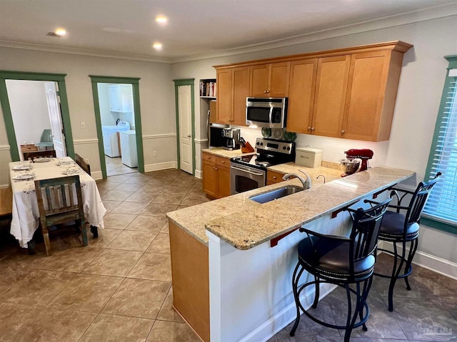 kitchen featuring a breakfast bar, independent washer and dryer, ornamental molding, sink, and stainless steel appliances