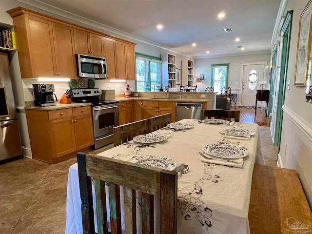 kitchen featuring kitchen peninsula, appliances with stainless steel finishes, light wood-type flooring, ornamental molding, and sink