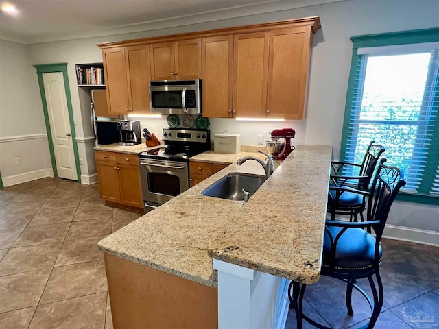 kitchen with a breakfast bar area, stainless steel appliances, sink, light tile patterned flooring, and light stone countertops