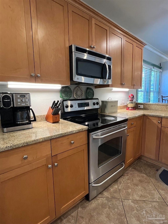 kitchen with crown molding, stainless steel appliances, light stone counters, and tile patterned flooring