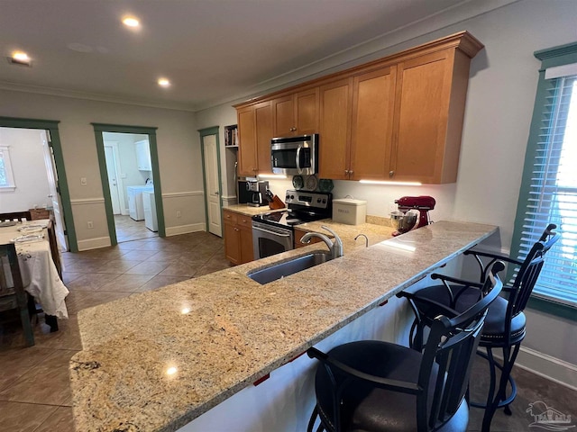 kitchen featuring a breakfast bar area, appliances with stainless steel finishes, washer and dryer, and kitchen peninsula