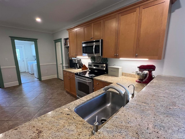 kitchen with appliances with stainless steel finishes, light stone countertops, independent washer and dryer, dark tile patterned flooring, and sink