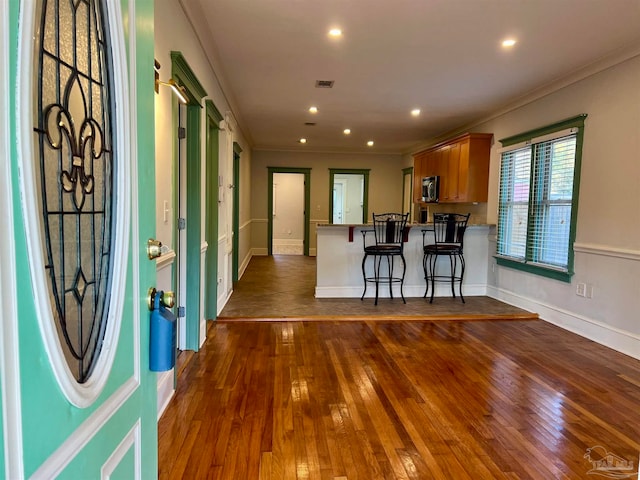 kitchen featuring kitchen peninsula, crown molding, a kitchen bar, and dark hardwood / wood-style flooring