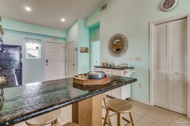 kitchen featuring a breakfast bar, white cabinets, dark stone counters, light tile patterned floors, and black fridge