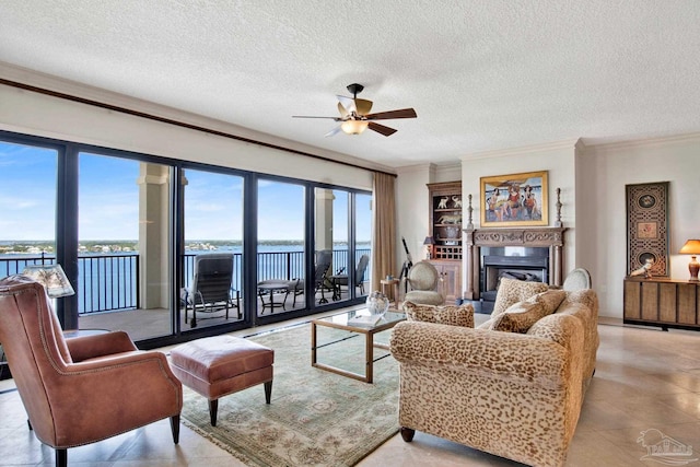 living area with a glass covered fireplace, ceiling fan, a water view, a textured ceiling, and crown molding