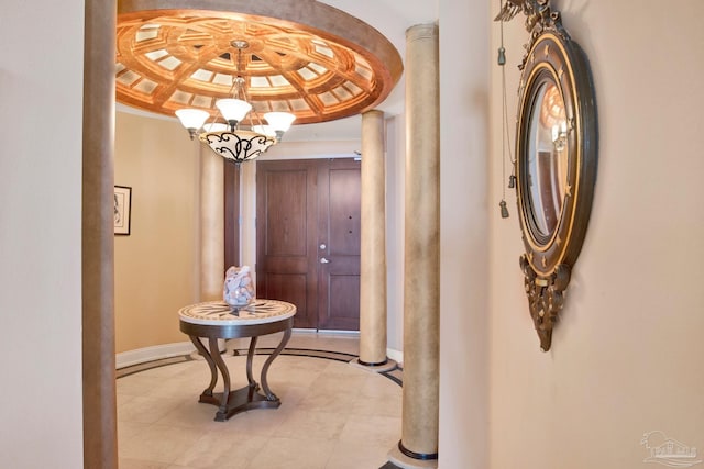 hallway with a notable chandelier, baseboards, a raised ceiling, decorative columns, and crown molding