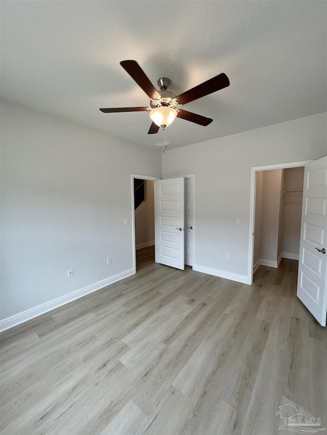 unfurnished bedroom with a spacious closet, a textured ceiling, light hardwood / wood-style flooring, a closet, and ceiling fan