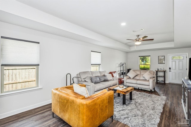 living room with a tray ceiling, dark wood-type flooring, and ceiling fan