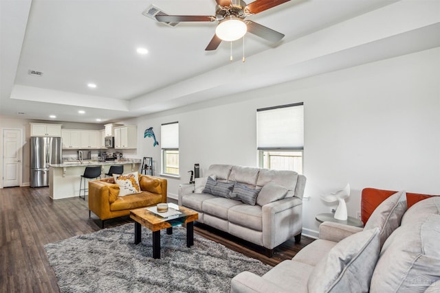 living room with dark hardwood / wood-style floors, a raised ceiling, and ceiling fan