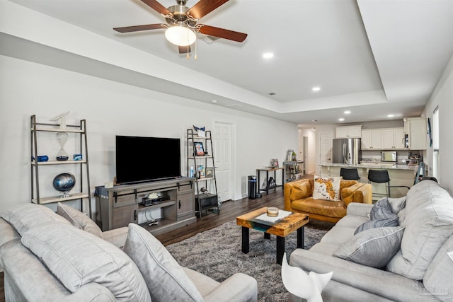 living room with ceiling fan, dark hardwood / wood-style flooring, and a raised ceiling