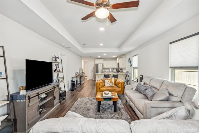 living room featuring dark hardwood / wood-style floors, a raised ceiling, and ceiling fan