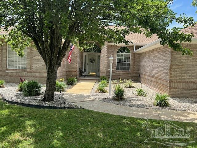 5140 Grumann Dr, Pensacola, FL 32507 - view of exterior entry featuring brick siding, a lawn, and roof with shingles