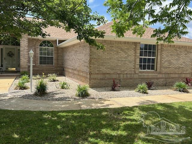5140 Grumann Dr, Pensacola, FL 32507 - view of side of property with brick siding, a shingled roof, and a lawn