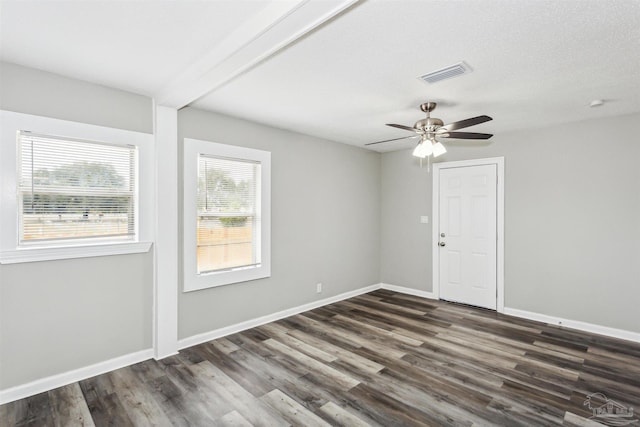 empty room featuring ceiling fan, dark hardwood / wood-style flooring, beam ceiling, and a textured ceiling