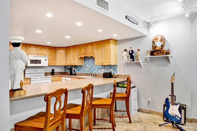 kitchen with white appliances, tasteful backsplash, a kitchen bar, kitchen peninsula, and sink