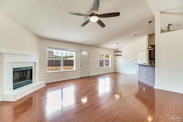 3086 Myrshine Dr, Pensacola, FL 32506 - unfurnished living room with a textured ceiling, a tiled fireplace, vaulted ceiling, wood finished floors, and ceiling fan
