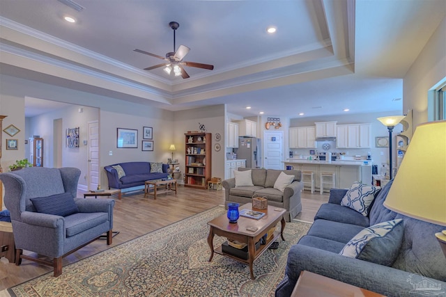 living room with crown molding, ceiling fan, light wood-type flooring, and a tray ceiling